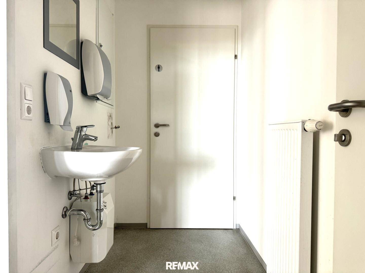 Kleiner, funktionaler Toilettenraum mit Waschbecken, Handtrocknern und weißer Tür.