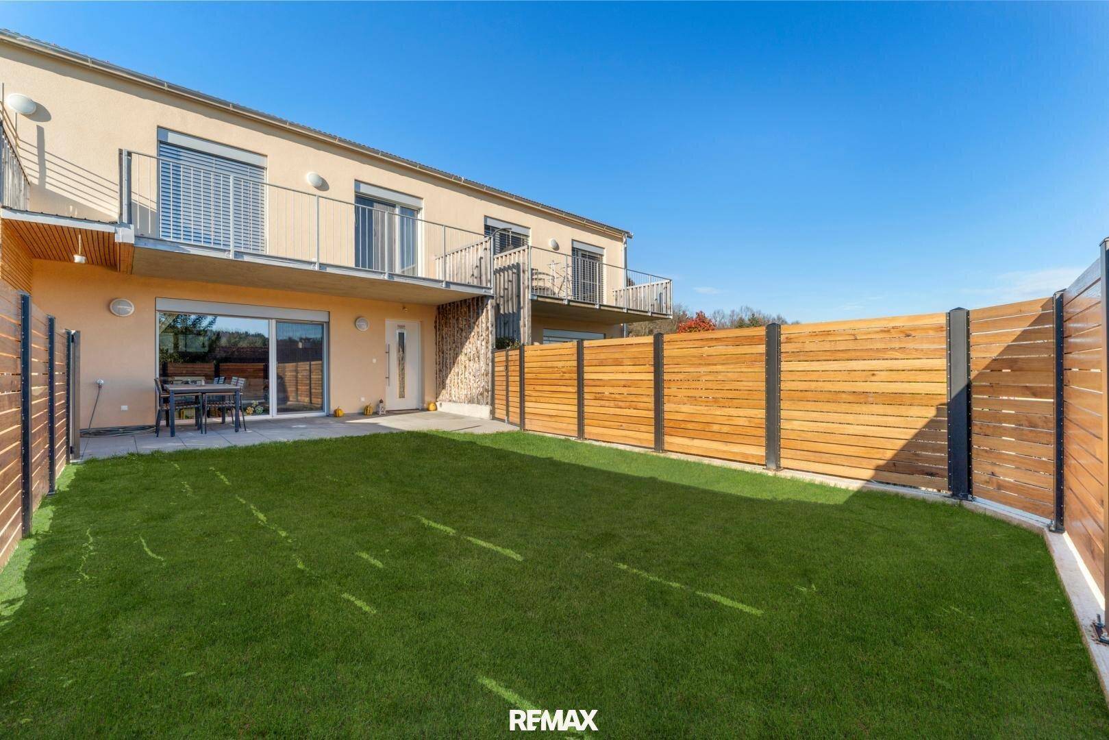 Gepflegter Garten mit Rasenfläche und Holzumzäunung hinter dem Haus.