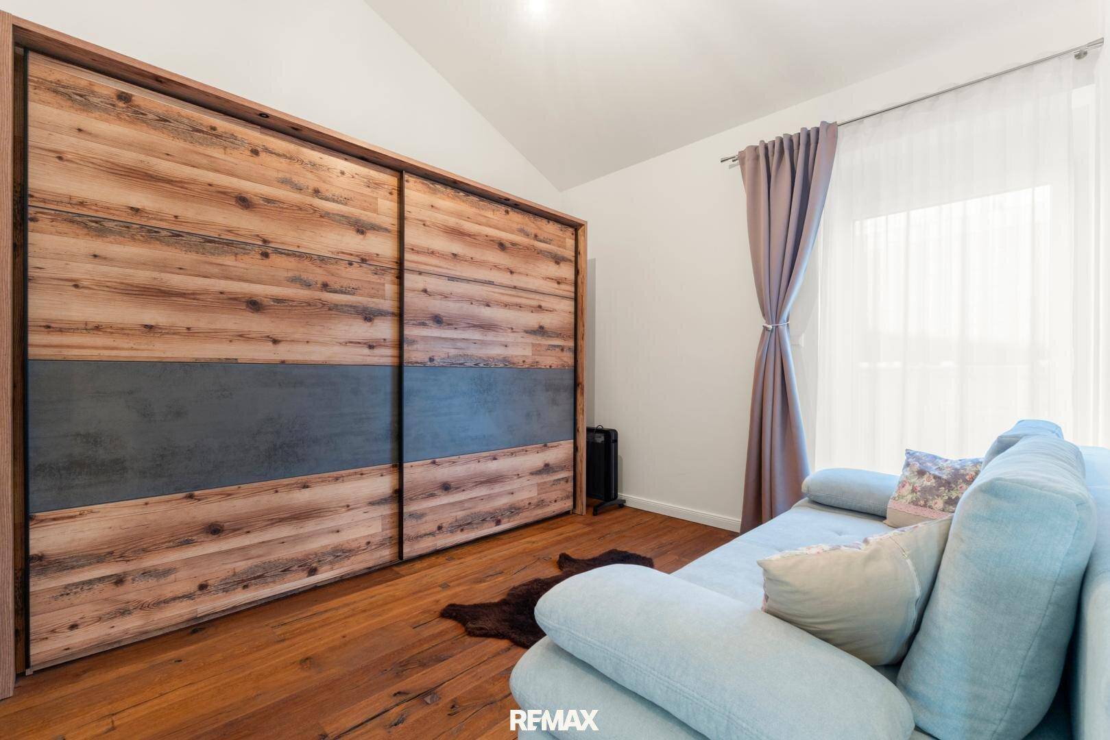Schlafzimmer mit großem Holzschrank, Sofa und Holzboden.