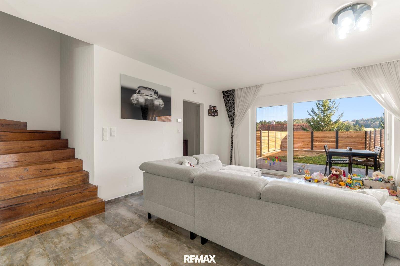 Helles Wohnzimmer mit bequemer Couch, Holztreppe und Zugang zum Garten.