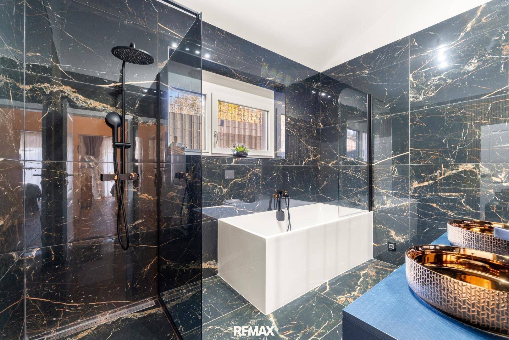 Luxuriöses Badezimmer mit schwarzem Marmor, Badewanne, Dusche und Fenster.