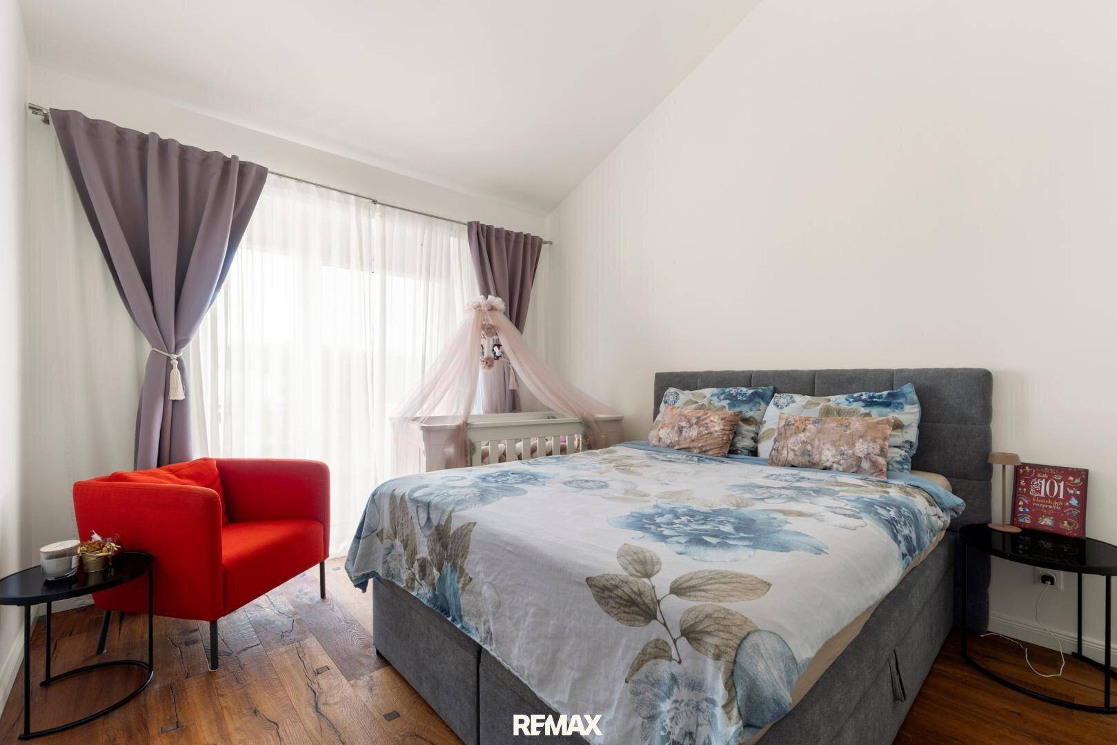 Gemütliches Schlafzimmer mit Doppelbett, rotem Sessel und Holzboden.