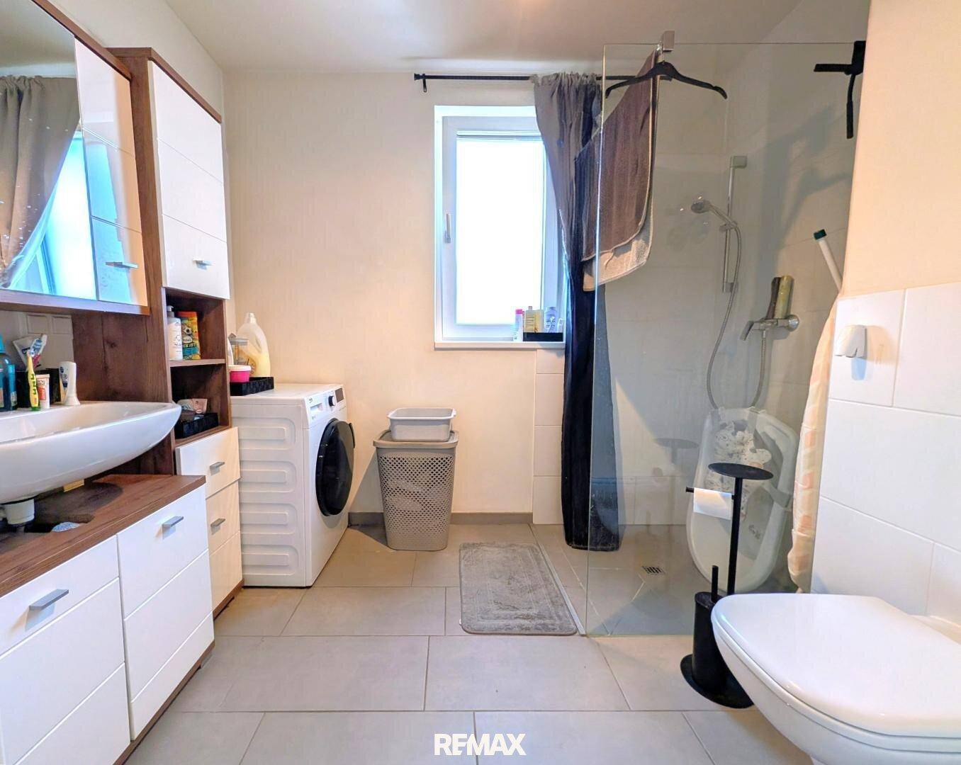 Helles Badezimmer mit begehbarer Dusche, Waschbecken, Toilette und Waschmaschine.