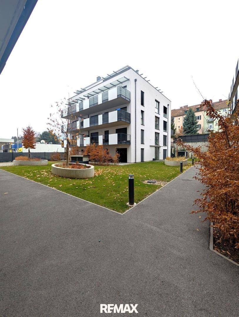 Modernes Mehrfamilienhaus mit Balkonen und gepflegter Grünanlage im Vordergrund.