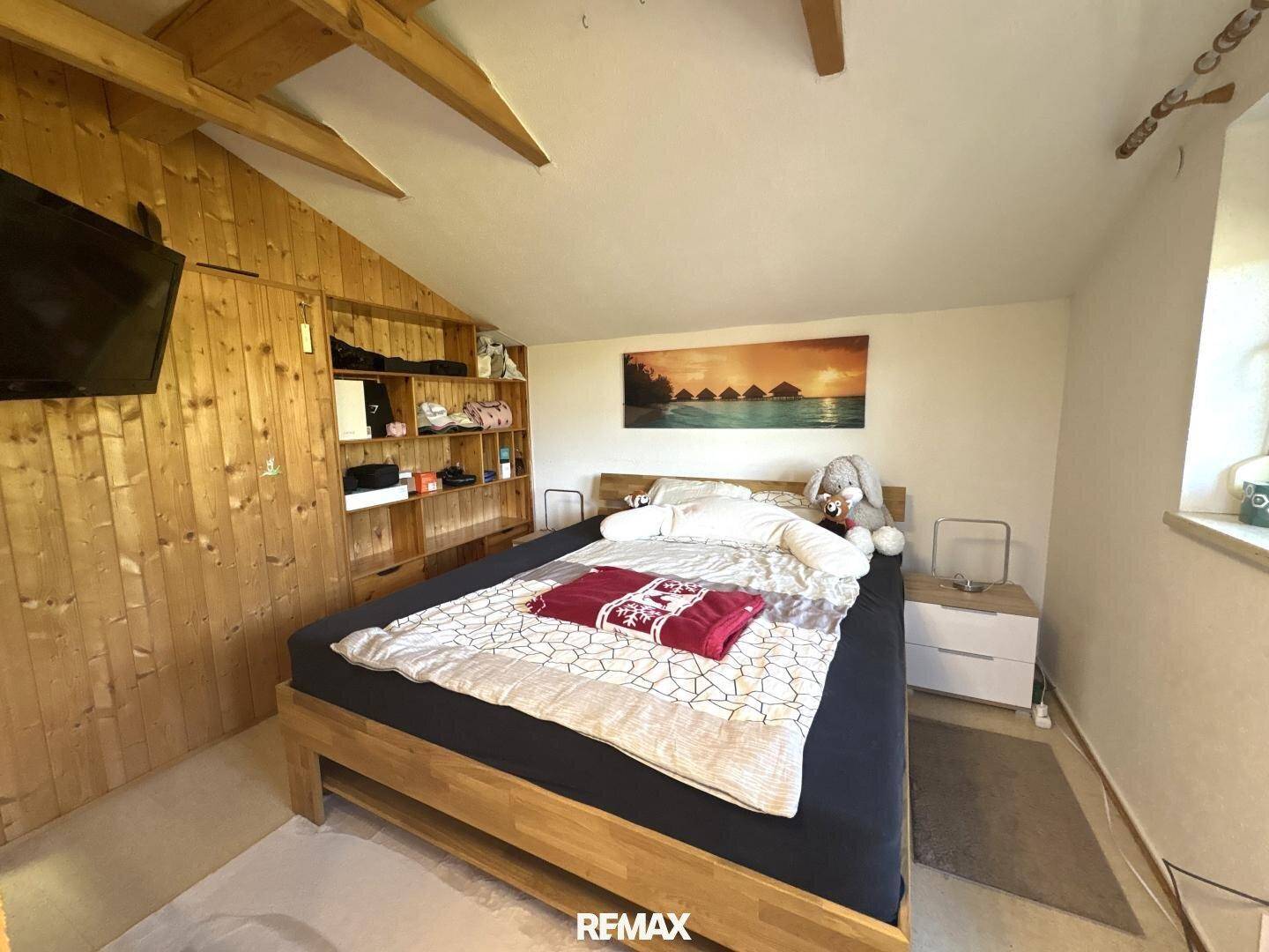Schlafzimmer im Dachgeschoss mit Holzwänden, sichtbaren Balken und einem Doppelbett.