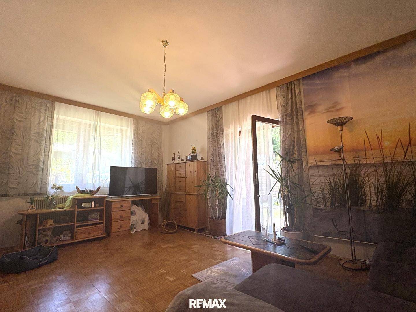 Helles Wohnzimmer mit Parkettboden, großen Fenstern und direktem Zugang zu einem Außenbereich.