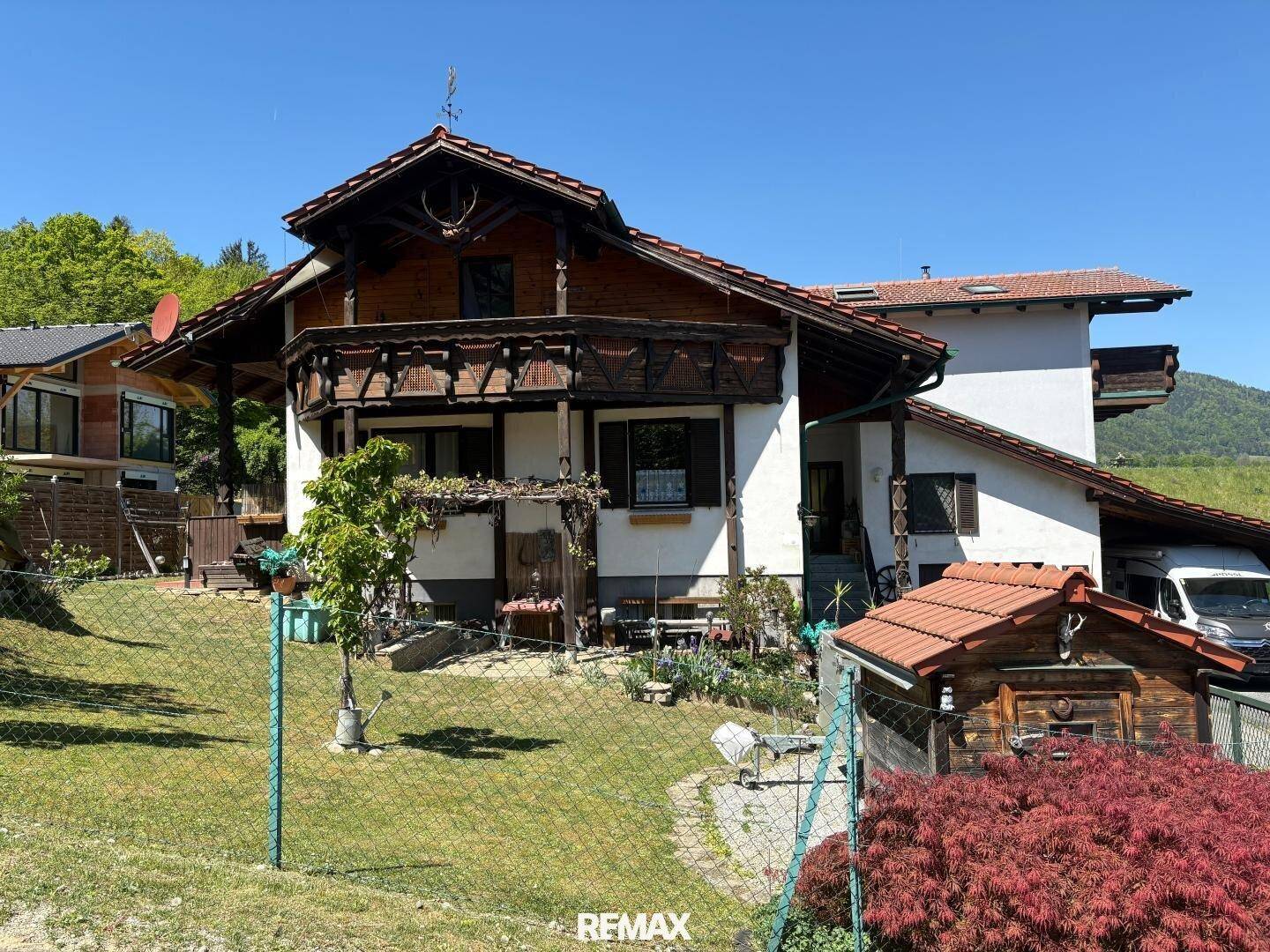 Traditionelles Wohnhaus mit Holzbalkonen und einem gepflegten Vorgarten unter blauem Himmel.