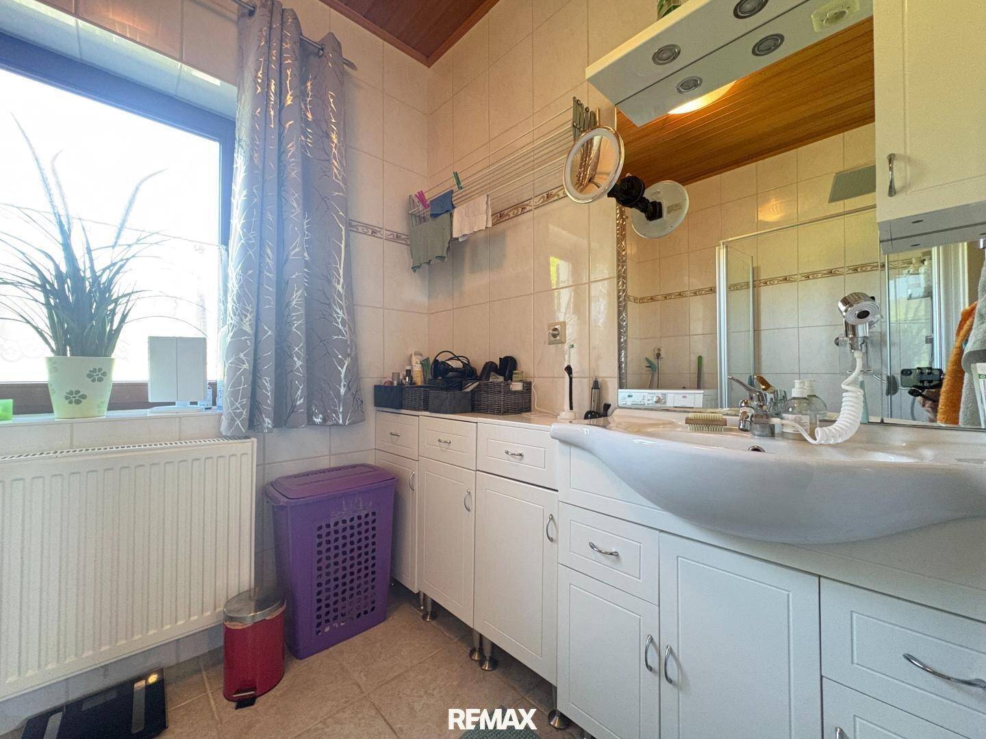 Badezimmer mit Waschtisch, Spiegelschrank und einem Fenster, das für natürliches Licht sorgt.