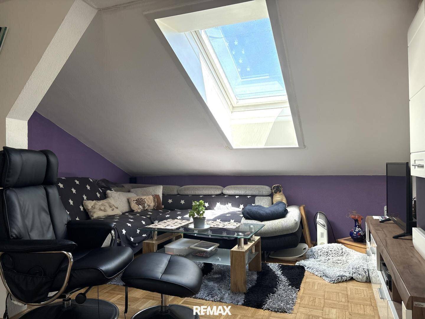 Gemütliches Wohnzimmer im Dachgeschoss mit Sofa, Couchtisch und großem Dachfenster für viel Helligkeit.