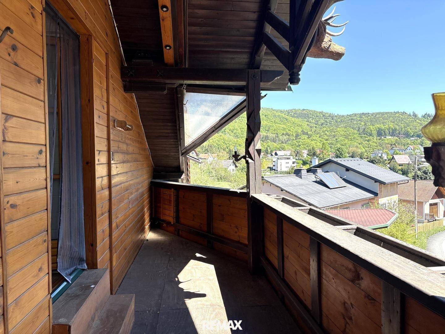 Rustikaler Holzbalkon mit Geländer und weitem Blick auf die umliegende grüne Landschaft.