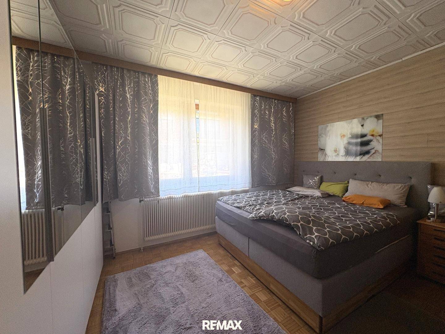 Gemütliches Schlafzimmer mit Doppelbett, Spiegelschrank und einem Fenster mit Vorhängen.