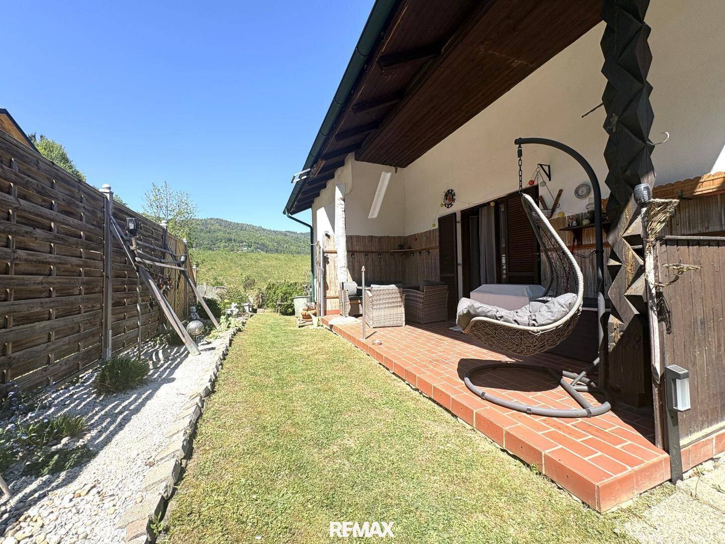 Kleine, gepflasterte Terrasse mit Hängesessel und Rasenfläche, ideal zum Entspannen im Freien.