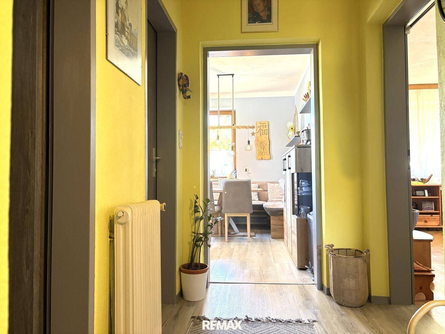 Heller Flur mit gelben Wänden und Laminatboden, der in den offenen Wohnbereich führt.