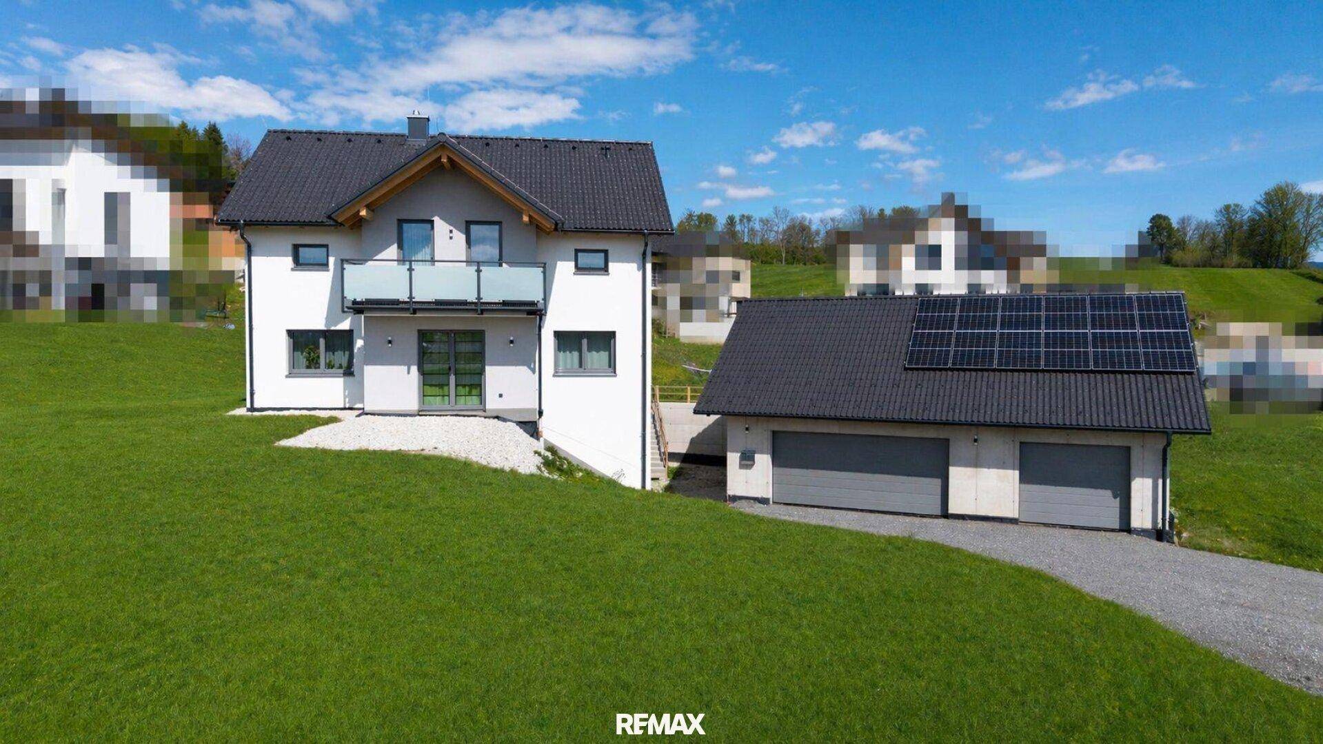 Vorderansicht des modernen Einfamilienhauses mit Balkon und Doppelgarage unter blauem Himmel.
