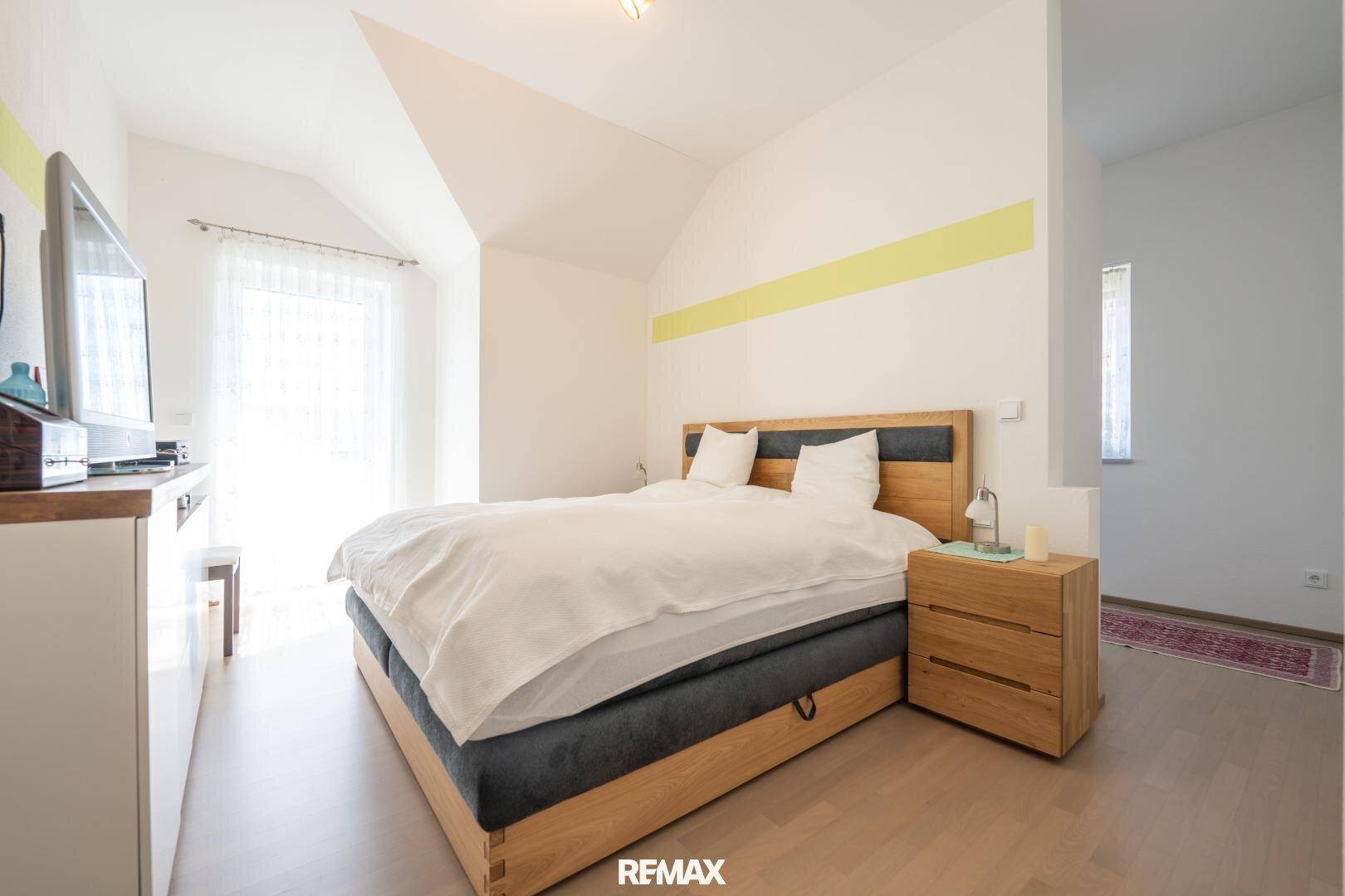 Gemütliches Schlafzimmer mit Holzbett, Dachschräge und Zugang zu einem Balkon.