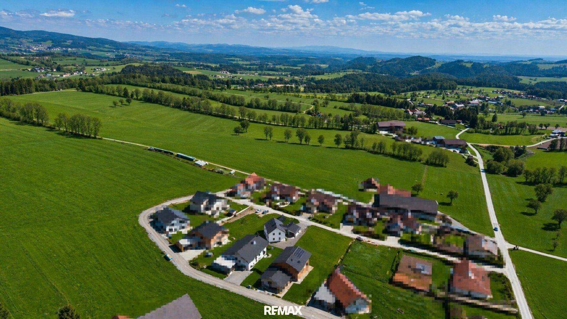 Panoramablick auf die ländliche Siedlung mit weiten grünen Feldern und bewaldeten Hügeln.