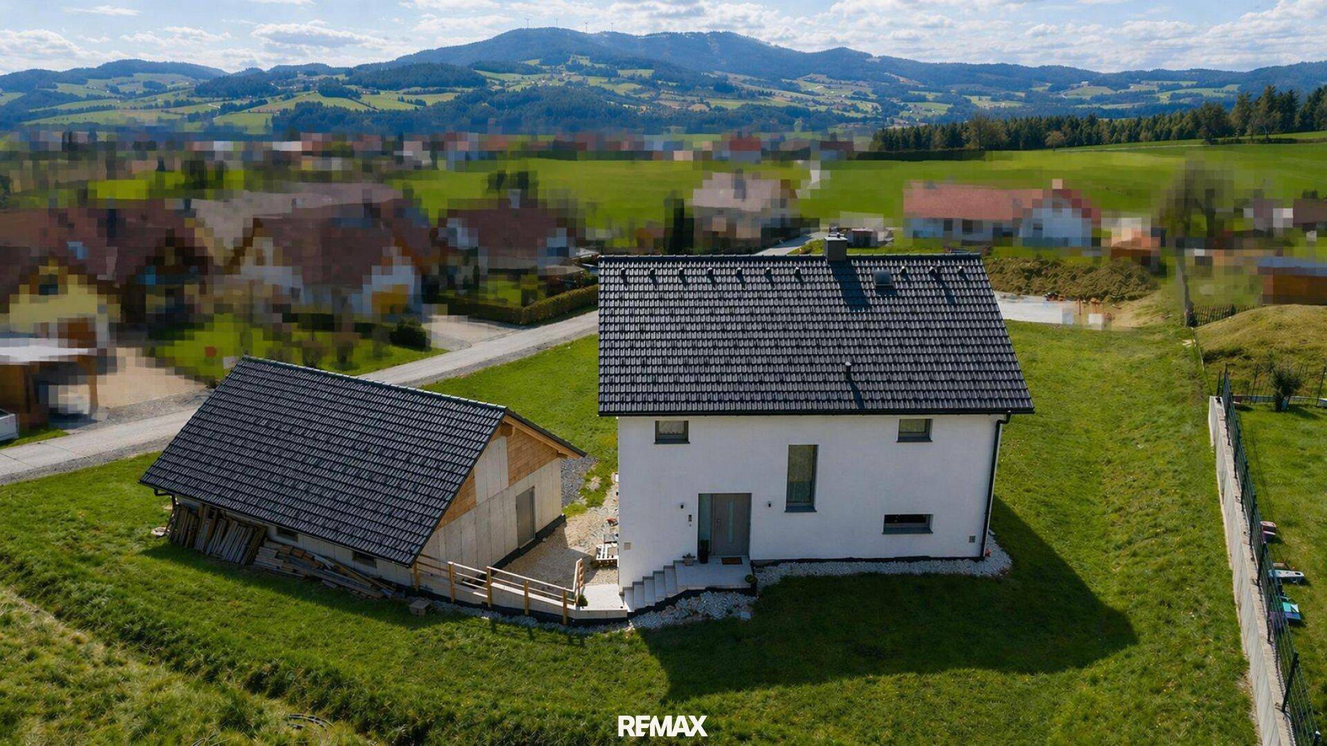 Rückansicht des Einfamilienhauses mit angrenzendem Nebengebäude auf einem grünen Hanggrundstück.