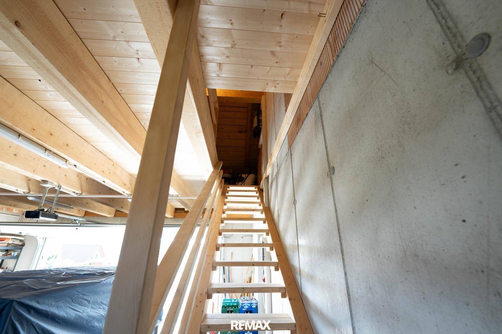Holztreppe führt zu einem ausgebauten Dachboden mit sichtbaren Holzbalken und -decken.