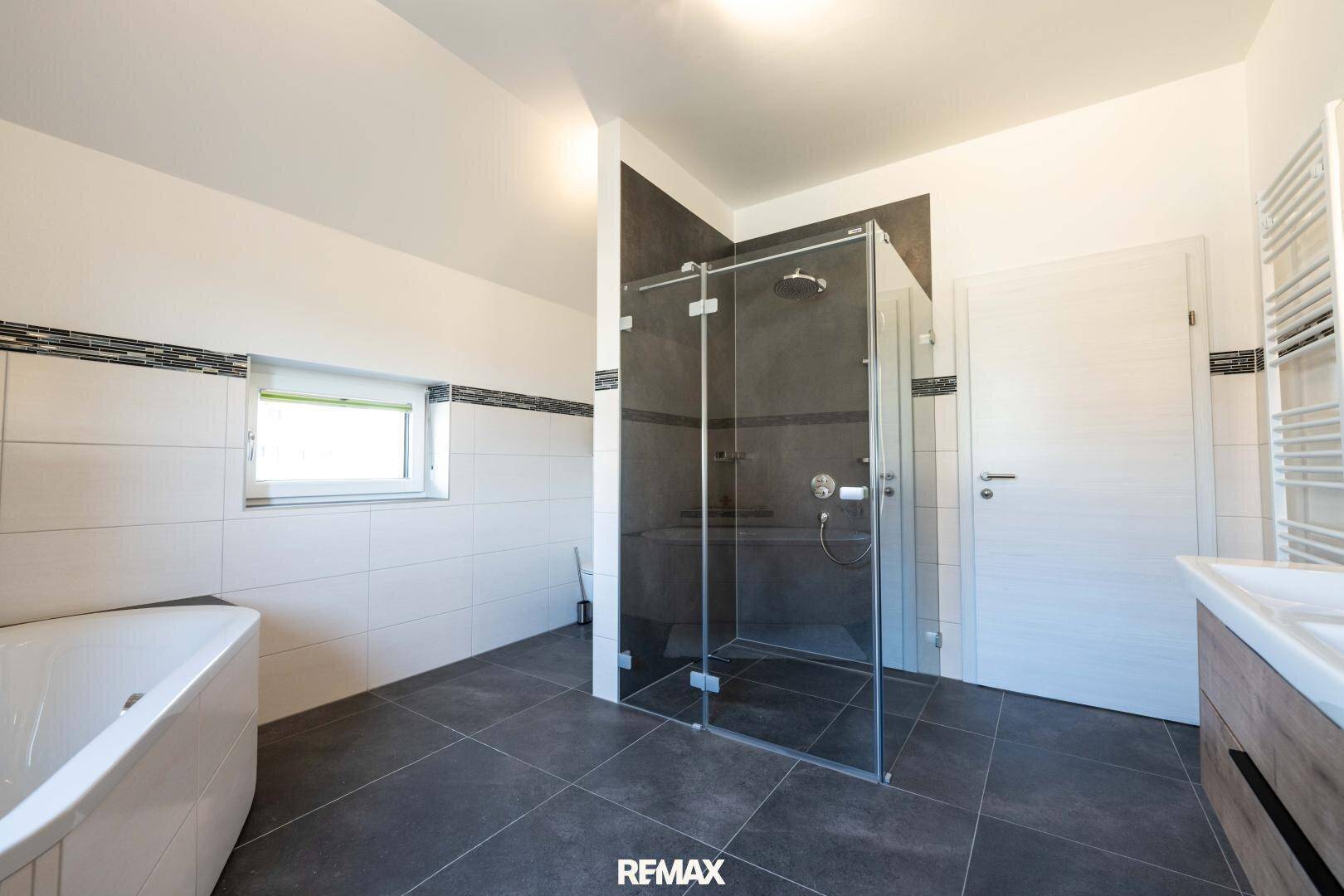 Helles Badezimmer mit großer begehbarer Dusche, Badewanne und Fenster.