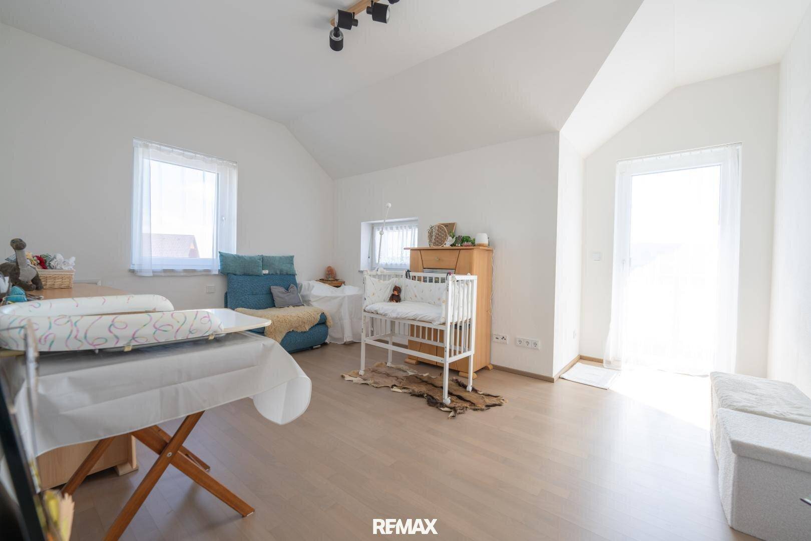 Freundliches Kinderzimmer mit Holzboden, Babybett und Zugang zu einem Balkon.