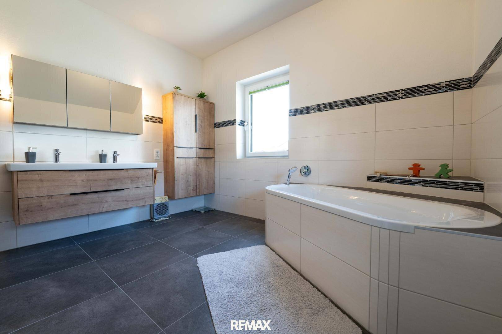 Modernes Badezimmer mit Doppelwaschbecken, Badewanne und dunklen Bodenfliesen.