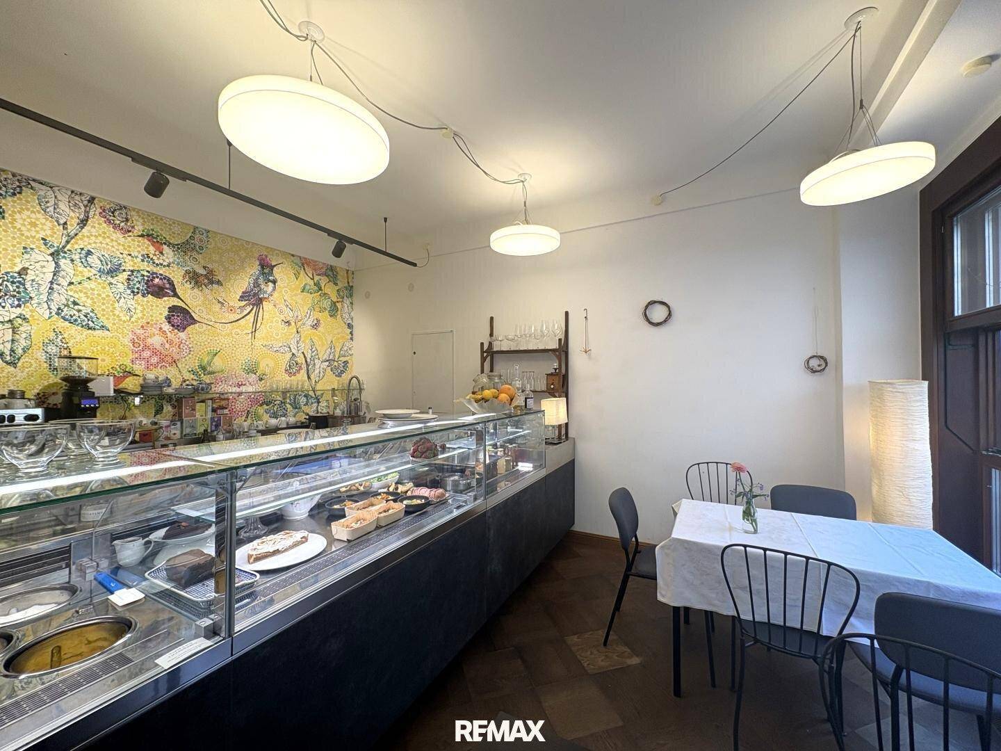Innenansicht eines Cafés mit einer langen Theke, Mosaikwand und schlichten Tischen.