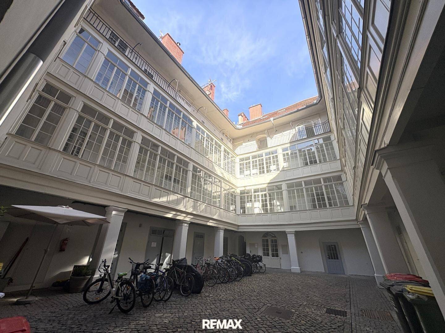 Historischer Innenhof eines Gebäudes mit vielen Fenstern, Balkonen und abgestellten Fahrrädern.
