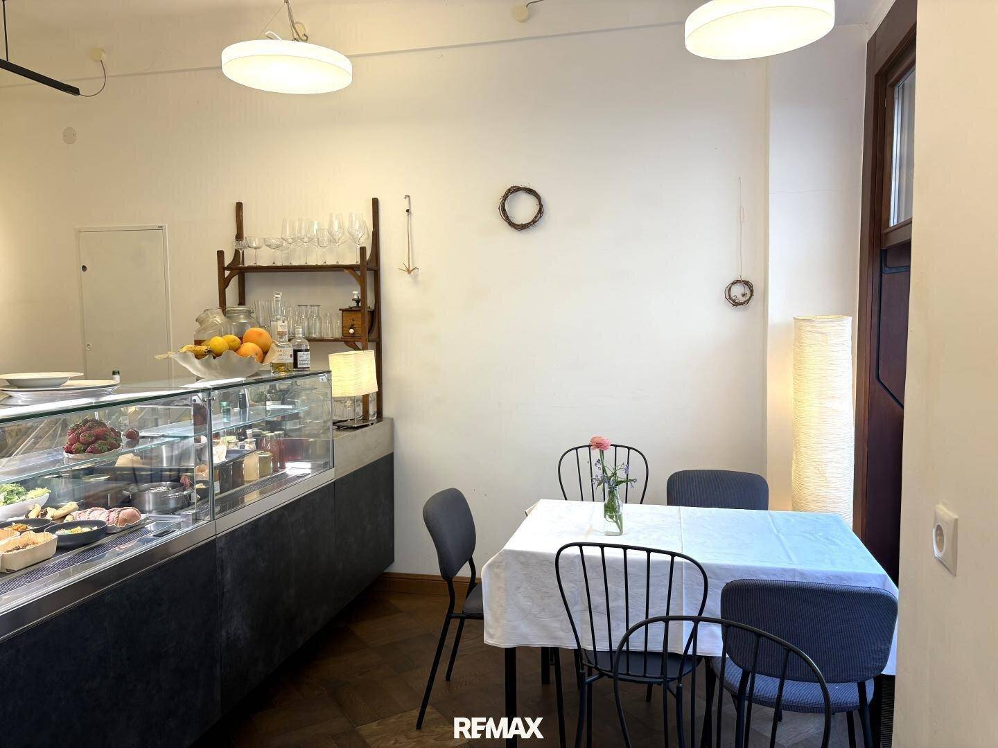 Gemütlicher Sitzbereich in einem Café mit einfachen Tischen, Stühlen und einer Theke im Hintergrund.