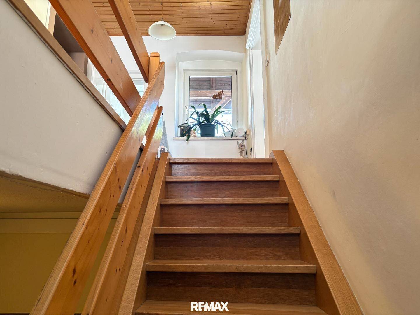 Holztreppe führt in die obere Etage, mit einem Fenster am Treppenabsatz für natürliches Licht.