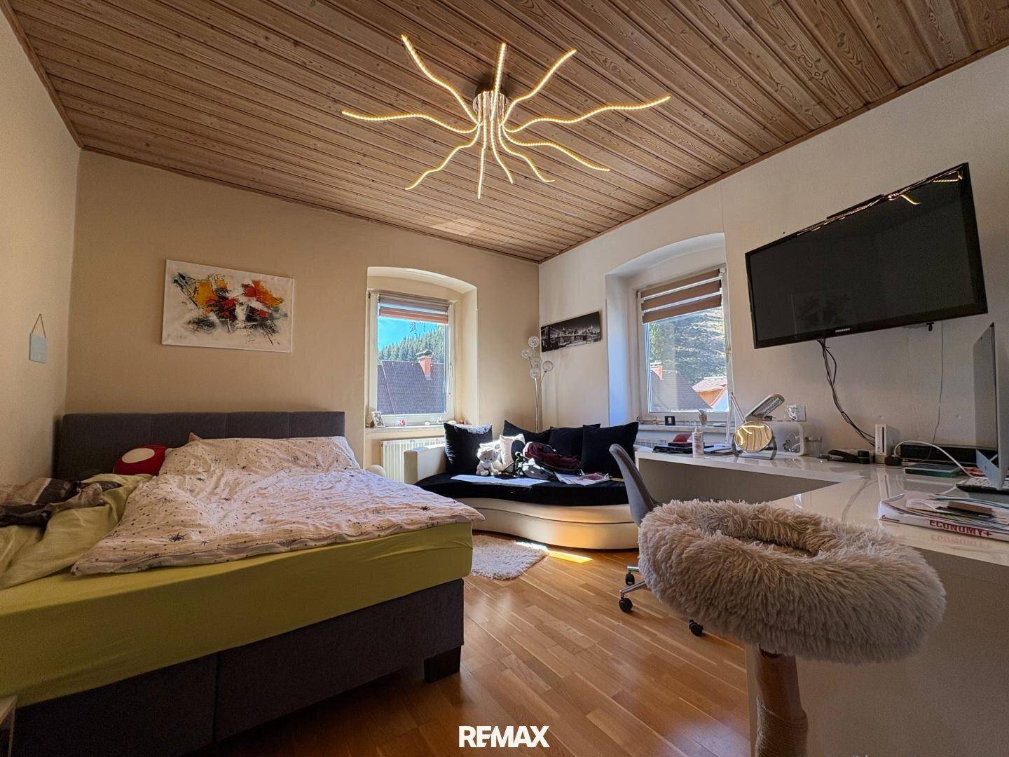 Helles Schlafzimmer mit Holzboden, zwei Fenstern und einem modernen Deckenlicht.