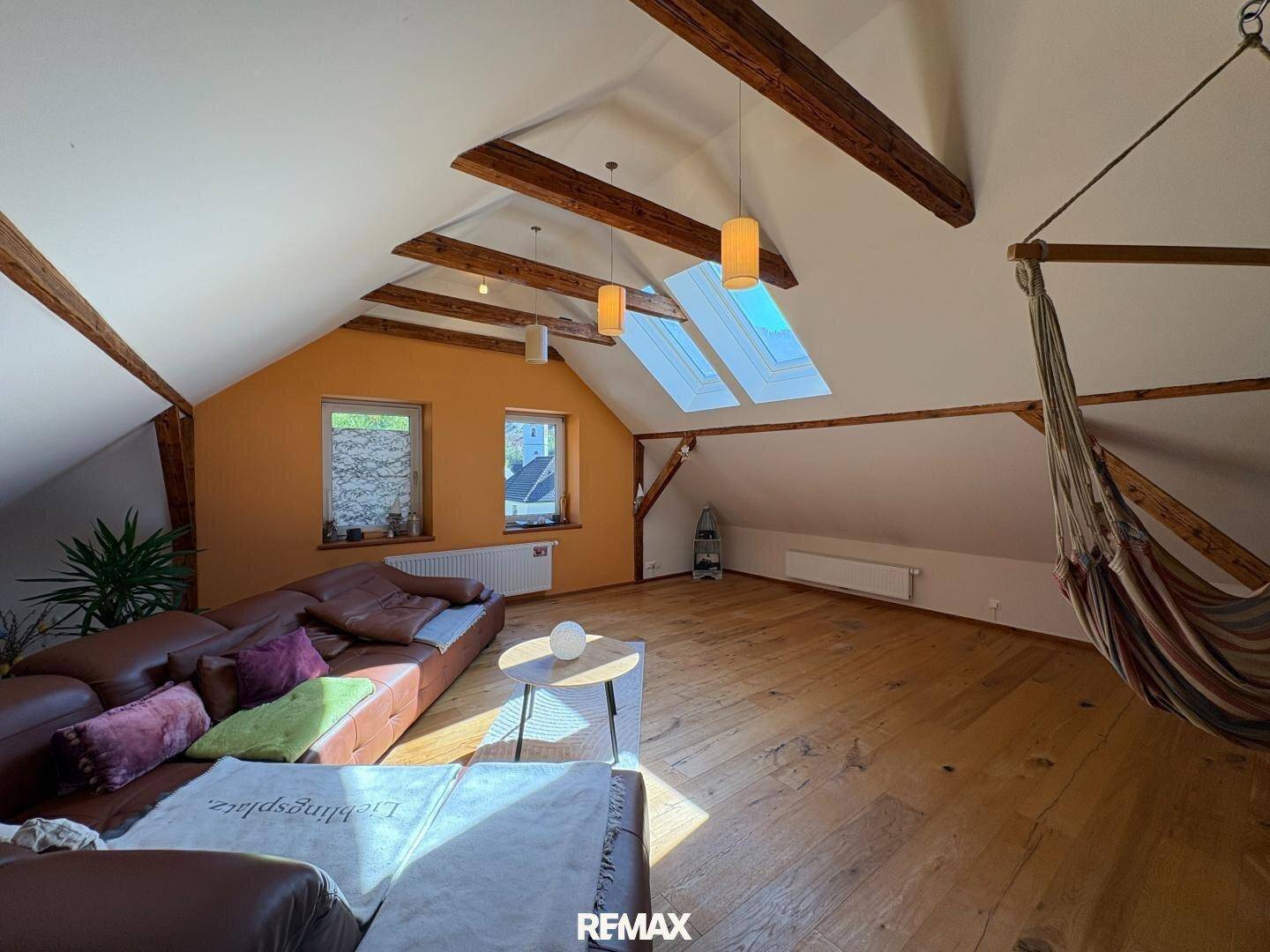 Geräumiger Dachboden-Wohnbereich mit Holzboden, gemütlicher Couch und Hängematte.