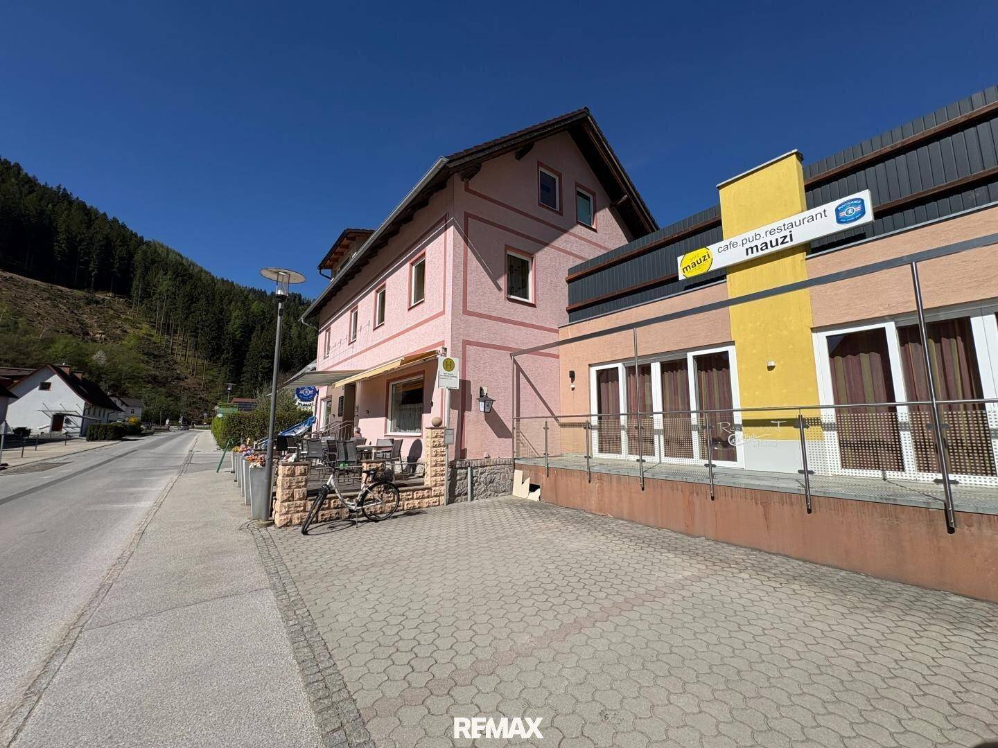 Gesamtansicht des Gebäudes mit rosa Fassade, angrenzendem gelbem Anbau und Parkplatz.