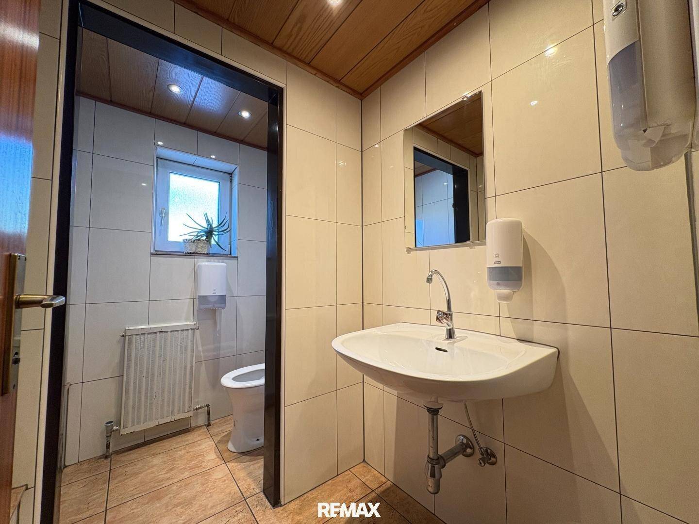 Gefliestes WC mit Waschbecken, Spiegel und Fenster, sauber und funktional.