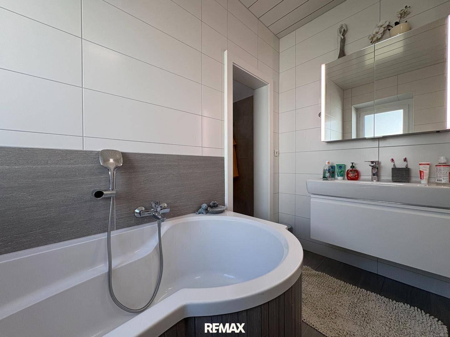 Modernes Badezimmer mit runder Badewanne, beleuchtetem Spiegelschrank und eleganten Fliesen.