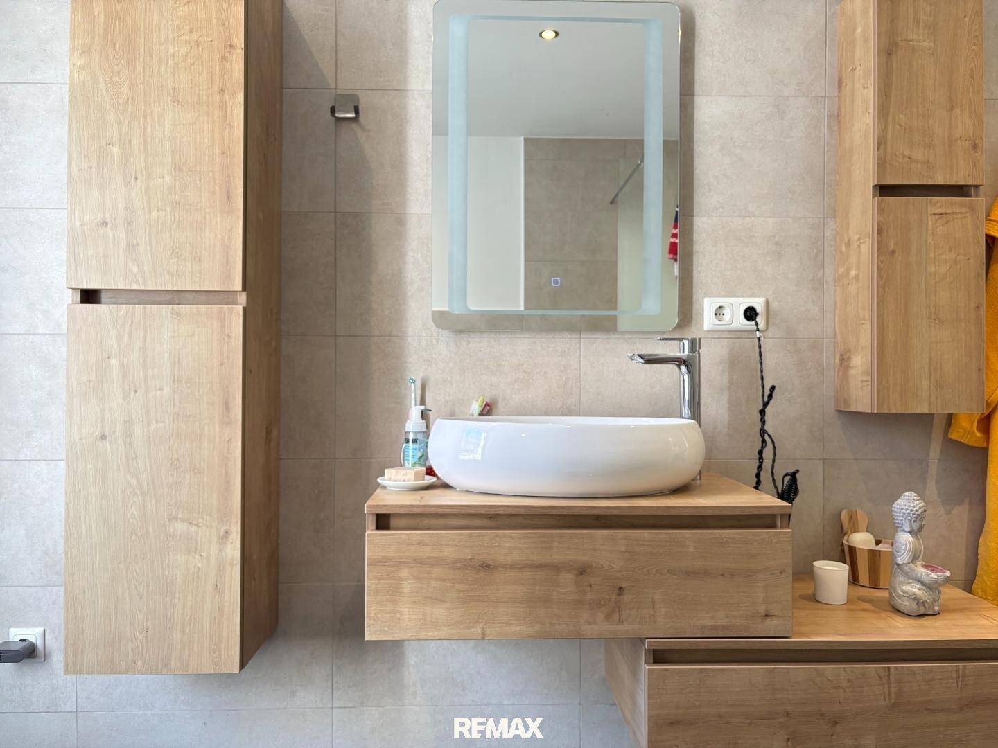 Modernes Badezimmer mit Holzwaschtisch, Aufsatzwaschbecken und beleuchtetem Spiegel.