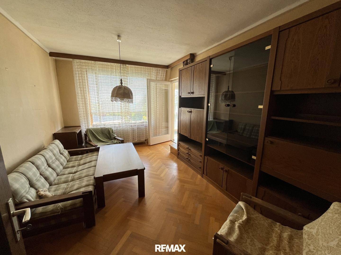 Gemütliches Wohnzimmer mit Parkettboden, großem Schrank und Blick ins Grüne.