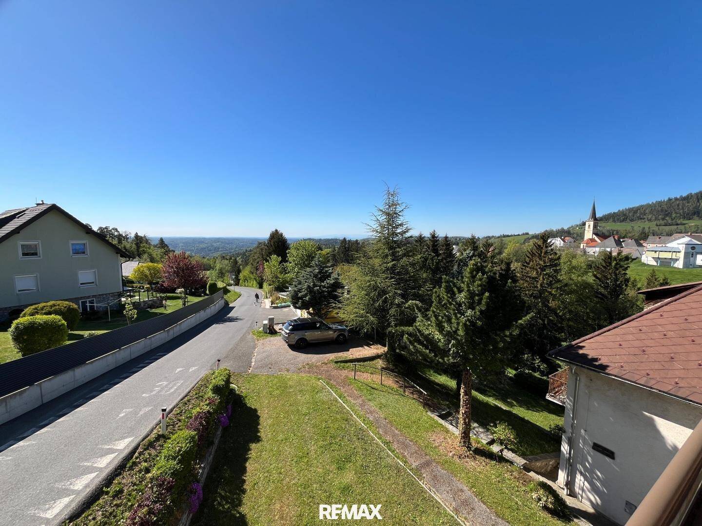 Weitläufiger Blick über die Landschaft mit einem Dorf und Bergen im Hintergrund.