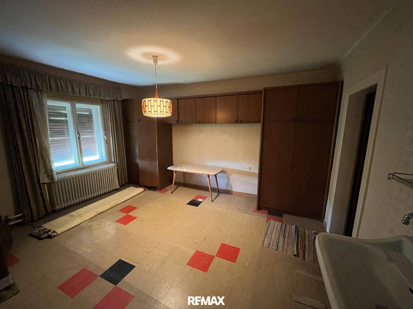 Geräumiger Raum mit alten Einbauschränken, einem Waschbecken und einem Fenster mit Heizkörper.