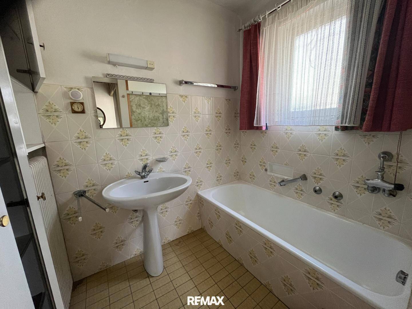 Badezimmer im 80er-Jahre-Stil mit Badewanne, Waschbecken und Fenster.