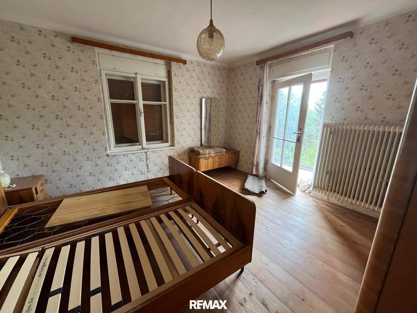 Schlafzimmer mit Holzdielenboden, floraler Tapete und Zugang zum Balkon.