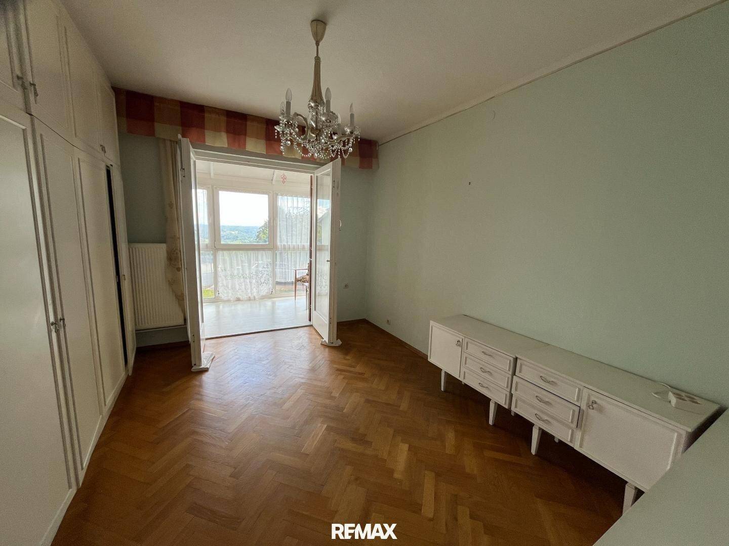 Schlafzimmer mit Parkettboden, Einbauschränken und Zugang zu einem Wintergarten.