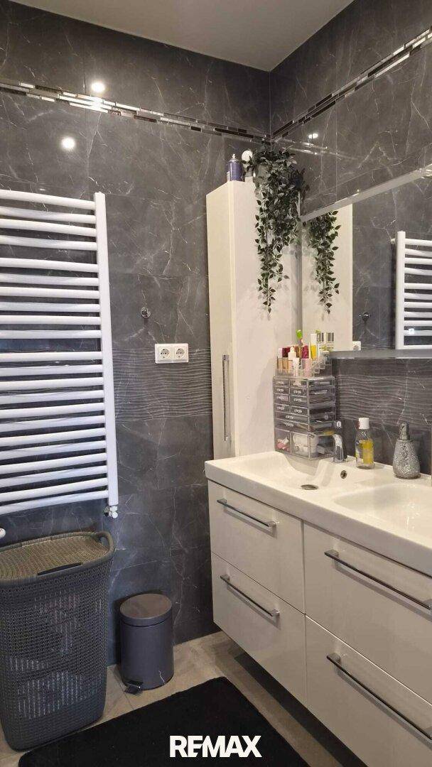 Modernes Badezimmer mit dunklen Fliesen, Doppelwaschbecken und beheiztem Handtuchhalter für Komfort.