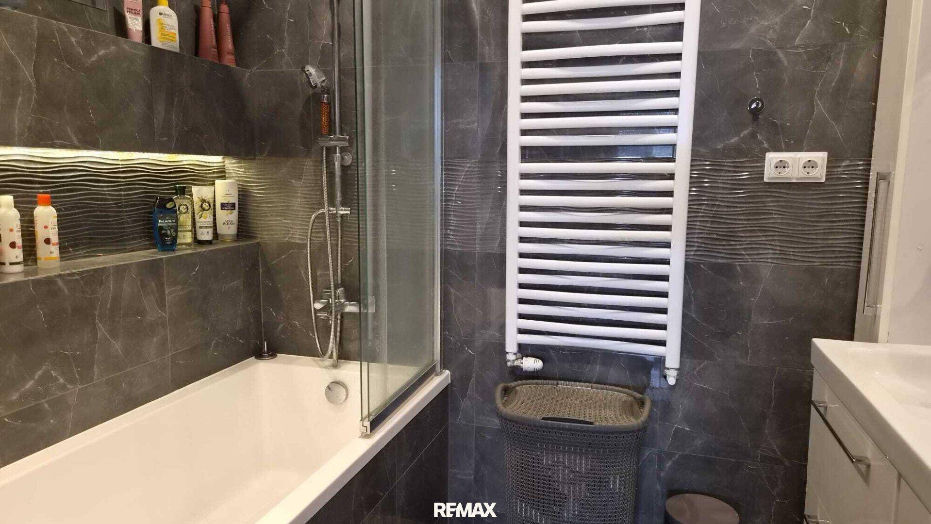 Elegantes Badezimmer mit Badewanne, Duschabtrennung und stilvollen dunklen Fliesen an den Wänden.