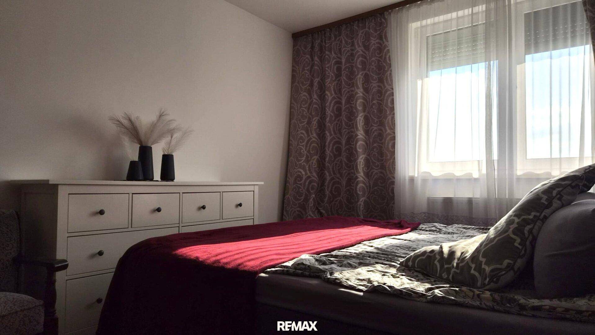 Helles Schlafzimmer mit Kommode, Doppelbett und Vorhängen für eine angenehme Atmosphäre und Privatsphäre.