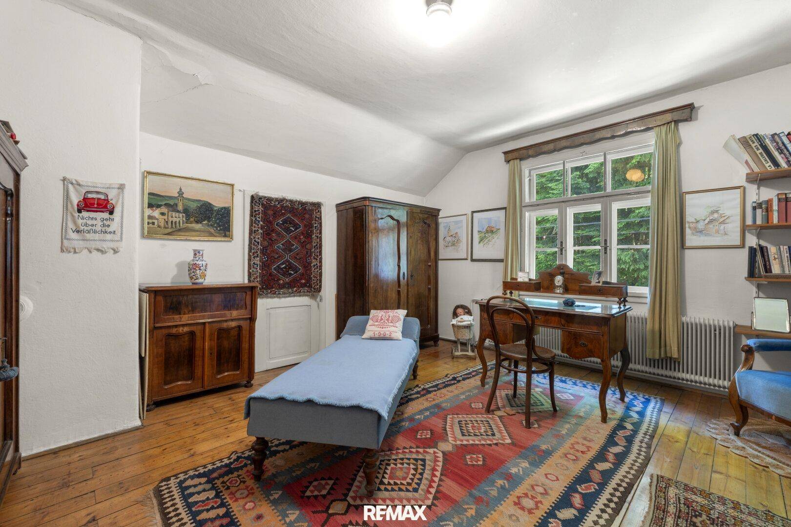 Helles Schlafzimmer mit Holzboden, traditionellen Möbeln und Blick ins Grüne durch das Fenster.