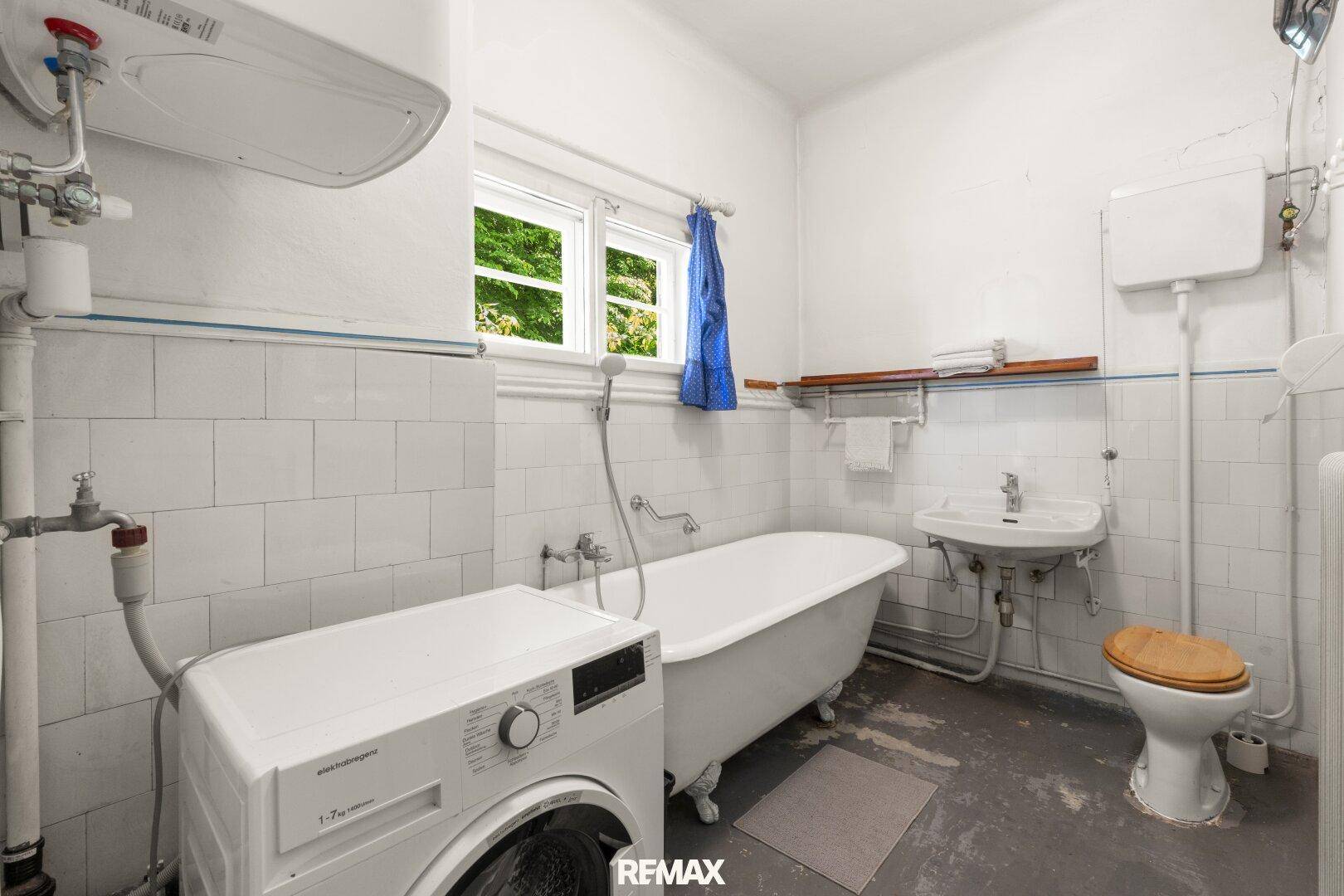 Einfaches Badezimmer mit Badewanne, Waschmaschine und Fenster, funktional eingerichtet.