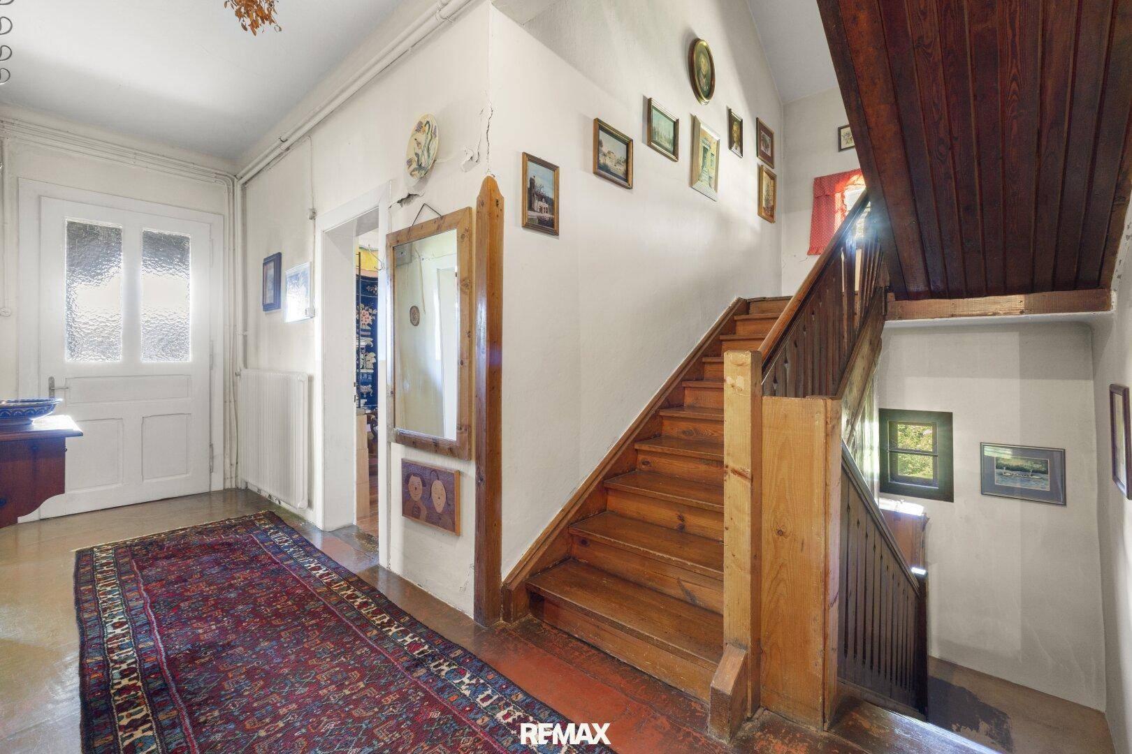 Geräumiger Flur mit Holztreppe und traditionellem Teppich, der die Stockwerke verbindet.