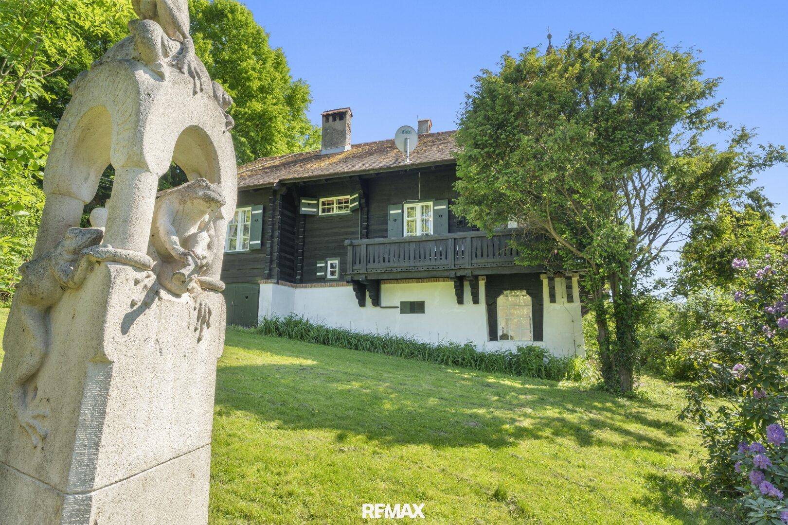 Historisches Holzhaus mit weitläufigem Garten und einer einzigartigen Steinskulptur, umgeben von Natur.