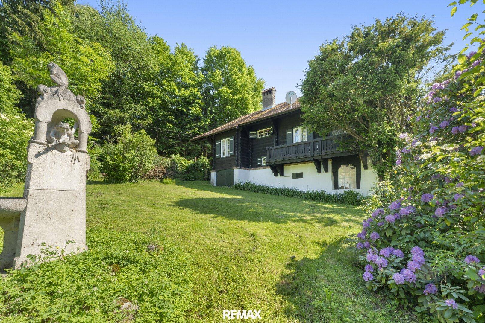 Idyllisches Holzhaus mit großem Garten und einer dekorativen Steinskulptur im Vordergrund.