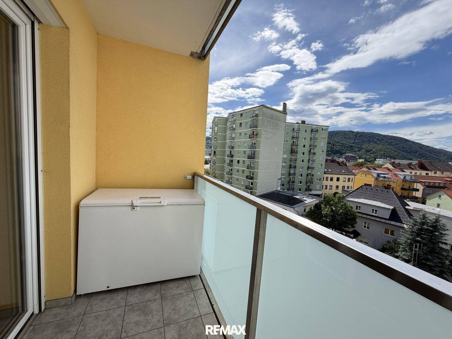 Balkon mit Fliesenboden und einer Gefriertruhe, umgeben von Stadtgebäuden.